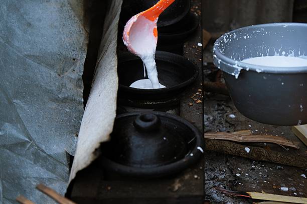 Traditional Indonesian serabi batter being poured into clay pan over fire. Authentic Asian street food cooking process.