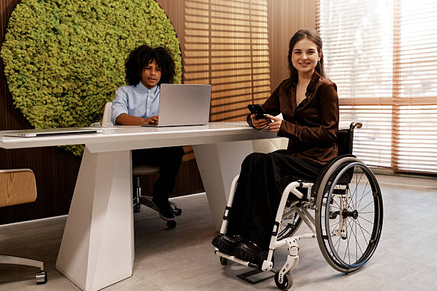istock Young woman in wheelchair using smartphone at modern office table 2255668973