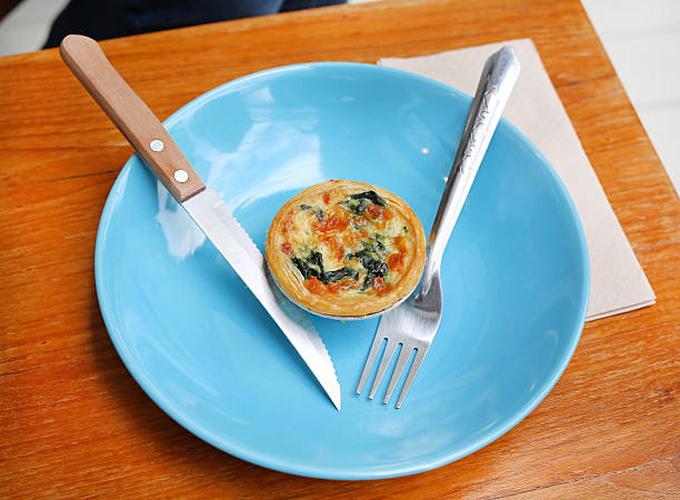 A delicious mini spinach quiche served on a vibrant blue plate with a knife and fork.