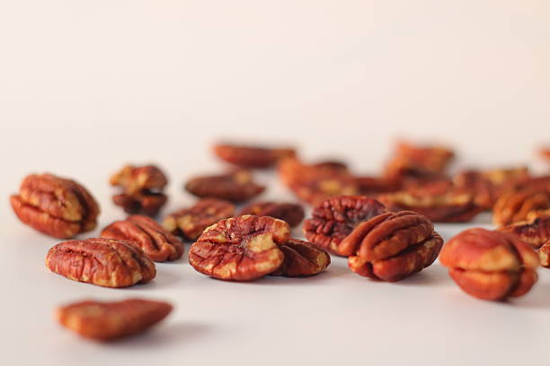 Pecan nuts presented in a natural scatter, featuring shelled pecan halves on a light surface. Close-up food image highlighting ridged texture, commonly used in desserts and baking across American cuisine