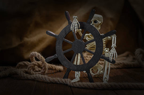 A conceptual still life featuring a skeleton figurine steering a vintage wooden helm, surrounded by nautical ropes and a moody, dark background.