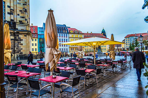 Dresden,Saxony,Germany-December 19 2014:a street scene in the historic city center Neumarkt square known for its baroque architecture. a moment of daily life with people walking on the wet, cobbled street under umbrellas on an overcast day.