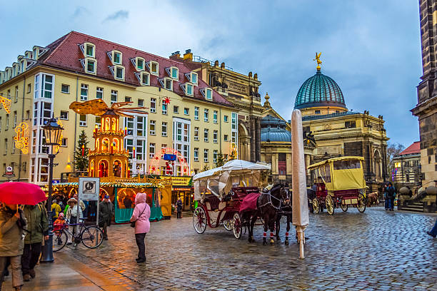 Dresden,Saxony,Germany-December 19 2014:a street scene in the historic city center Neumarkt square known for its baroque architecture. a moment of daily life with people walking on the wet, cobbled street under umbrellas on an overcast day.