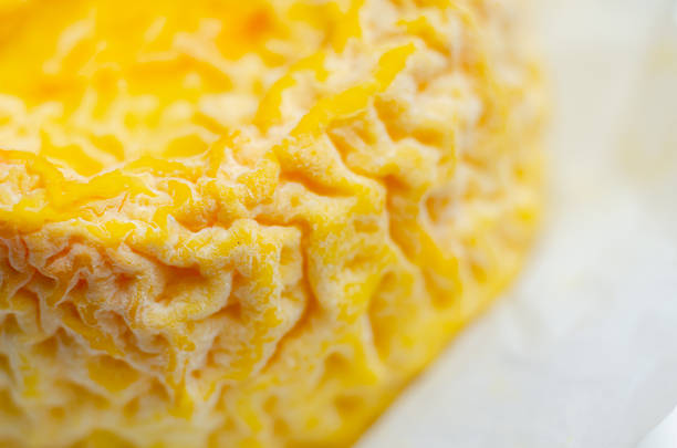 A yellow cheese is sitting in a paper wrapper, popular soft french cheeses