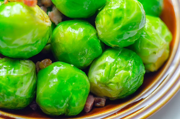 A plate of green brussels sprouts with bacon on top. The bacon is spread out over the sprouts, giving them a savory and slightly crispy texture