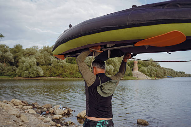 On a tranquil river bank, rafters of all ages revel in the unique experience of sliding down an overturned raft, their joy harmonizing with nature's calm.