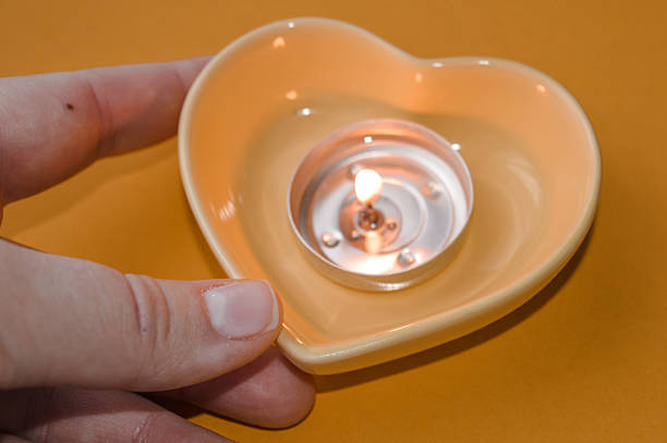 Lit tealight candle in a heart-shaped ceramic holder held in a hand on a warm monochrome yellow background, creating a cozy and romantic Valentine’s Day atmosphere.