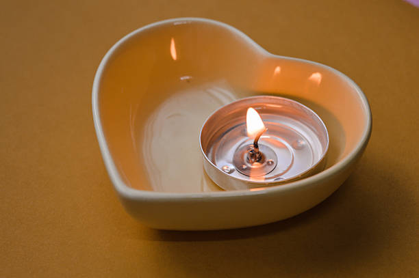 Lit tealight candle in a heart-shaped ceramic holder held in a hand on a warm monochrome yellow background, creating a cozy and romantic Valentine’s Day atmosphere.