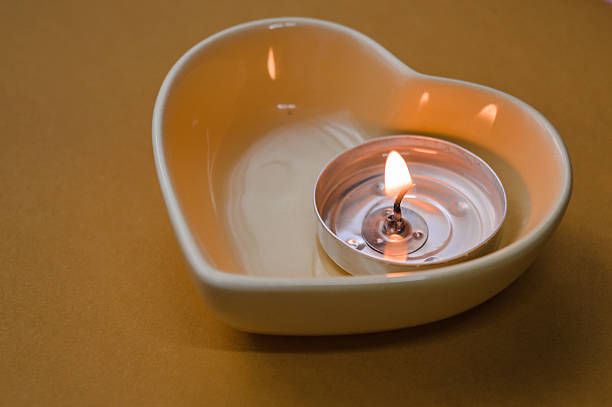 Lit tealight candle in a heart-shaped ceramic holder held in a hand on a warm monochrome yellow background, creating a cozy and romantic Valentine’s Day atmosphere.