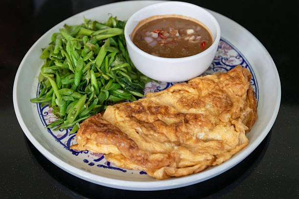 Golden omelet with sauteed morning glory and spicy dipping sauce, savory homecooked meal with vibrant greens and rich condiment