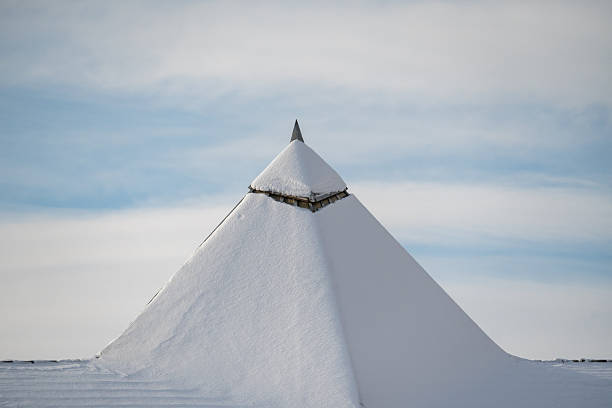 Minimalist winter image showing a snow covered roof peak against a pale blue sky. The photograph highlights cold weather conditions, snow accumulation, winter climate and architectural details of a residential building during freezing temperatures. Suitable for editorial use related to winter weather, climate and seasonal conditions.