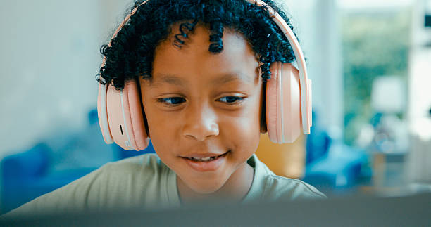 istock Young African-American boy wearing headphones, is deeply focused while participating in online learning session from home. Education courses online. 2255691481