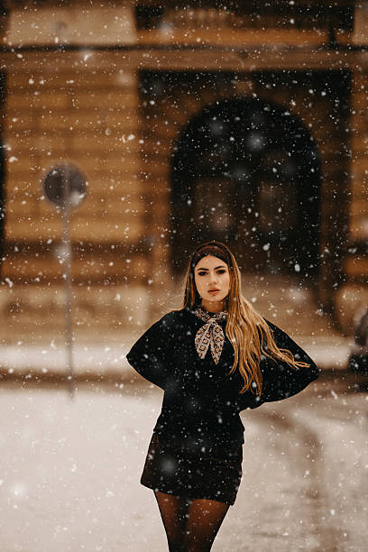 Young adult woman standing in a city during a winter snowfall looking at camera