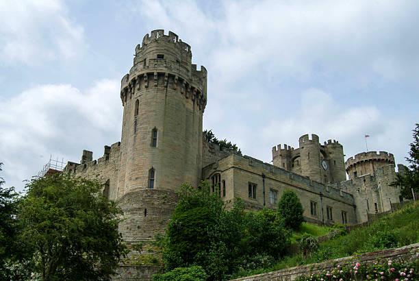 The historic tower of St. Mary's Church in Warwick, England, with its Gothic spires and clock faces, rises above the townscape and lush countryside. A prominent symbol of Warwick's heritage.