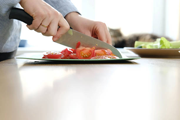 Preparing fresh colorful salad. Morning kitchen activity with fresh vegetables meal. Casual home cooking. Chopping carrots, lettuce in cozy setting. Hands slicing fruits on green board. Clean eating