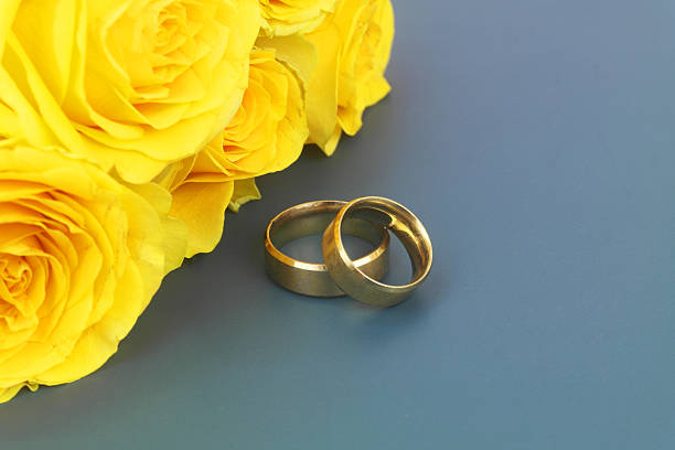 Yellow roses bouquet with gold wedding rings on blue background. Copy space for text.