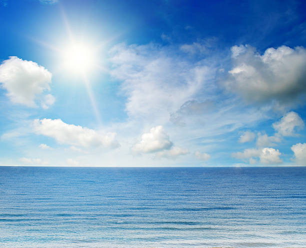 A calm blue ocean meets a bright sunny sky filled with soft white clouds. This tranquil seascape offers a peaceful mood and ample copy space for travel and vacation-themed designs.