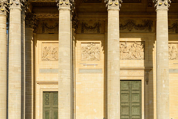 Front view of tall Corinthian columns and sculpted stone reliefs on the Pantheon facade in Paris, illuminated by warm sunlight and casting soft shadows on the historic architecture.