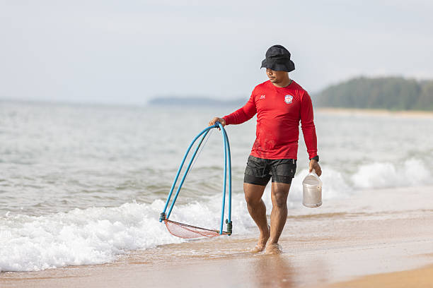 14 November 2025, Mai Khao Beach - Phuket.Young Thai man is walking on the beach for hunting fish.Phuket Island - Thailand.