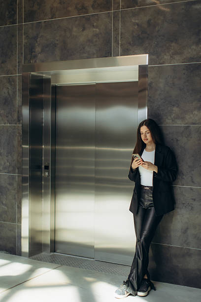 istock Woman Waiting by Elevator Using Smartphone in Modern Business Setting 2255720298