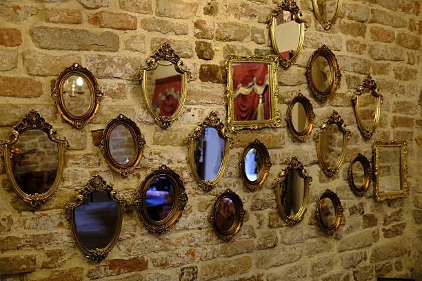 Collection of ornate antique-style mirrors arranged on an exposed brick wall in Venice, Italy. The gilded frames and warm interior lighting reflect traditional Venetian decorative design, historic textures, and elegant interior architecture.