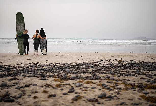 istock Female Surfers Standing on Beach Facing the Ocean 2255726261