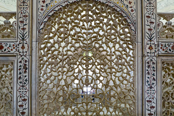 Delicate marble jali screen featuring floral and geometric patterns, framed by ornate inlaid borders within the mausoleum interior of the Taj Mahal in Agra. Soft natural light highlights the craftsmanship and detailed carvings.