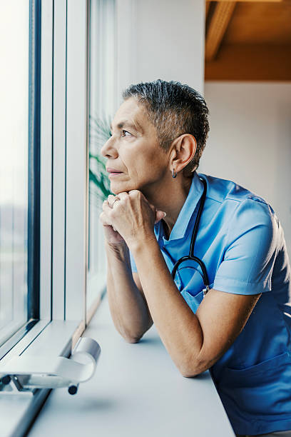 istock Healthcare worker looking thoughtful through window wearing scrubs 2255746480