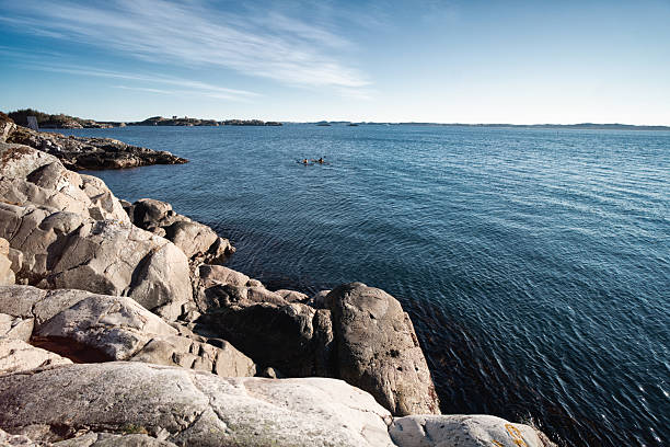 Wide view of a rocky coastline overlooking calm blue sea on a clear day, with small islands visible on the horizon. Natural coastal landscape conveying tranquility, open space, and connection with nature. Ideal for travel, outdoor lifestyle, and environmental concepts.