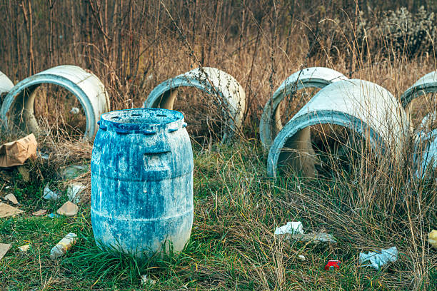 Abandoned blue plastic barrel and concrete pipes in overgrown meadow, selective focus
