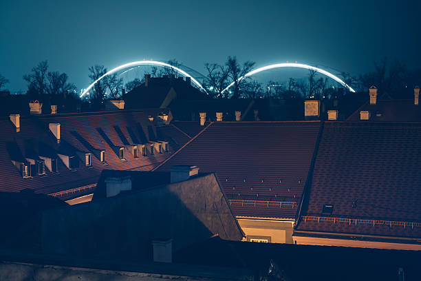 Illuminated Zezelj Bridge arches over rooftops in Petrovaradin, Novi Sad at night, selective focus