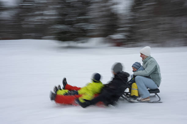 Family is sledding down a hill during winter, enjoying a cold day outdoors with elements of speed and motion blur.