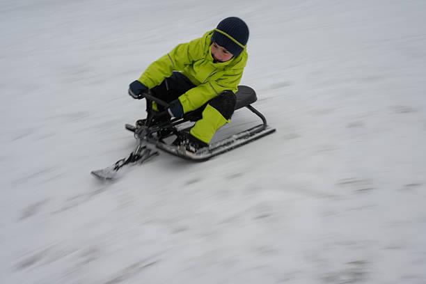 Young boy is enjoying a thrilling ride on a sled, speeding down a snowy slope during winter, creating motion blur.