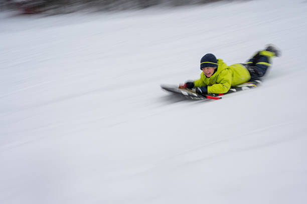 Young boy is sledding fast down a snowy hill, experiencing the joy and thrill of winter sports with motion blur.