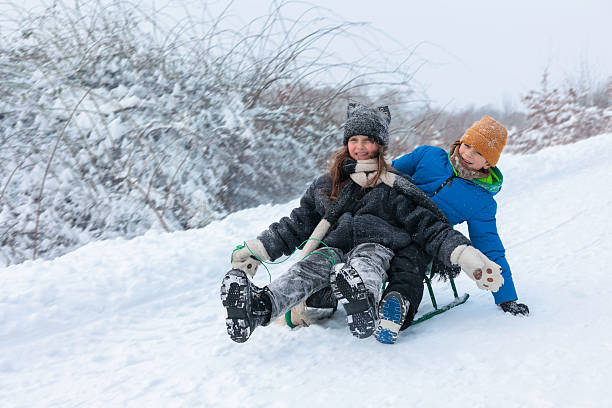 A small group of school-aged children are seen riding on a wooden toboggan as they enjoy some fun outside on a cool Winters day.  They are each dressed warmly in winter clothing and appear to be having fun.