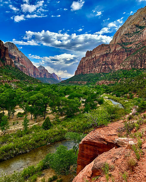 Stones balanced in the waters of The Narrows in Zion National Park.  Red sandstone background.  Tree with yellow leaves. The time of year is Autumn.