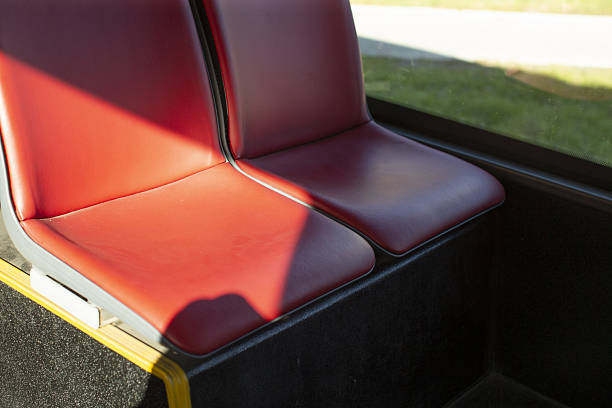Empty red bus seats flooded sunlight smooth vinyl upholstery reflects warm morning glow, yellow trim accenting edge, window hint