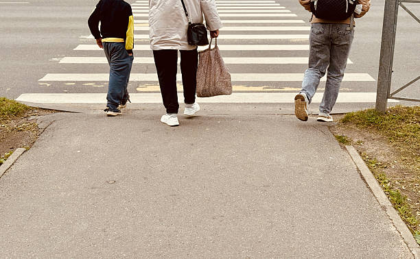 Group Walking Away From Crosswalk Sidewalk, Three Figures Backview, Casual Clothing, Patterned Tote, Warm Tones, Curbside Perspective, Candid Weekend Stroll, Social Connection, Relaxed Pace,