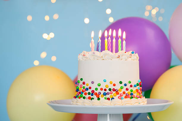 istock Delicious bento cake with colorful sprinkles and burning candles on light blue background against blurred lights, closeup 2255772666