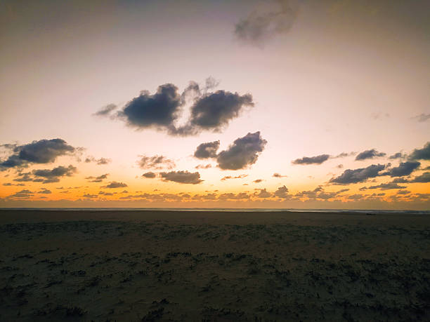 Capture the serene essence of a tranquil beach at twilight. Dramatic clouds float over a vibrant orange horizon, evoking a sense of solitude and peace. Ideal for calming backgrounds.