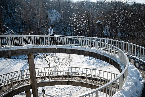 Man running on a snowy spiral pedestrian bridge. Showing winter fitness, exercise and healthy active lifestyle outdoors