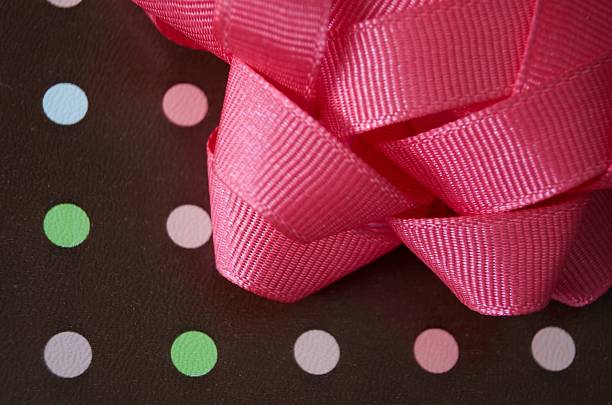 Brown wrapping paper with green, pink, blue and purple polka dots is adorned with a full pink bow.  Close up shot of a portion of the present, showing details