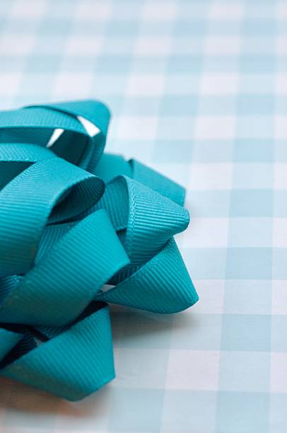 Wrapping paper with light blue and white checks and a fabric teal or turquoise coloured bow. The shot is a close up and only a portion of the present and the bow are visible