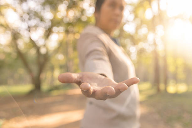An outstretched hand reaching out with an open palm in a sunny park. This conceptual image represents support, trust, guidance and offering help or kindness amidst a warm, bokeh forest background.