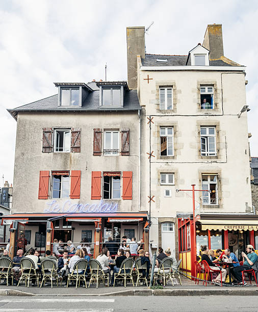 People gather at pavement cafes  among historic stone buildings in Saint-Malo, Brittany, capturing everyday summer life in a coastal French town.