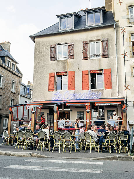 People gather at pavement cafes  among historic stone buildings in Saint-Malo, Brittany, capturing everyday summer life in a coastal French town.