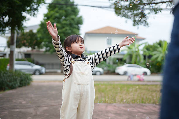 Asian girl playing with bubbles outdoors at the park. Cheerful childhood moment showing freedom.