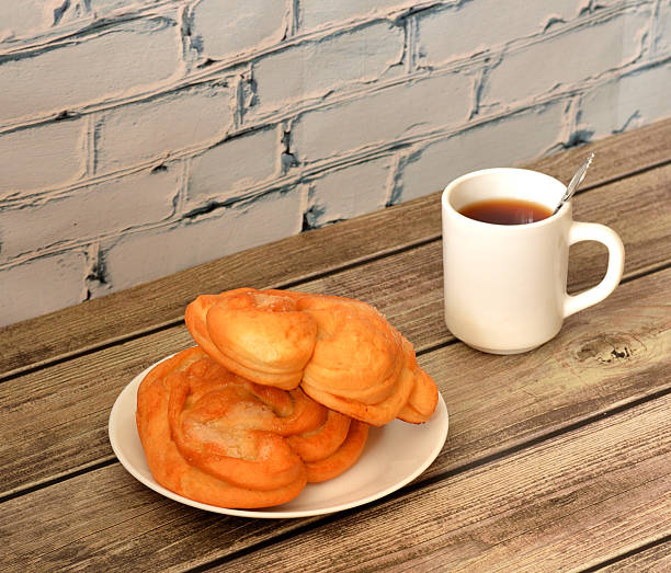 Two sugar pretzels on a plate and a cup of hot black tea on a wooden table.