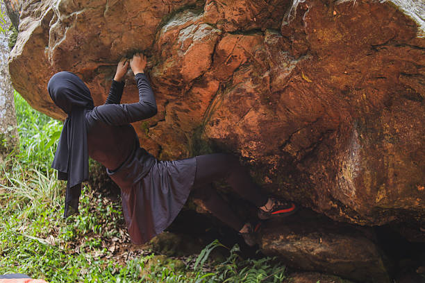 Portrait of Cute Girl rock Climber hanging on vertical orange wall energetic passionate Face Expression elegant Pose looking up orange and blue colour Stone Formations