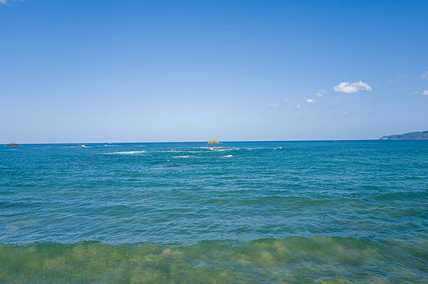 Vivid turquoise water stretches toward the horizon at Shotenkyo Beach in Kumihamacho, with scattered rocky islets and a clear blue sky creating a peaceful coastal scene.